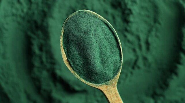 Heap of green spirulina algae powder in a wooden spoon, top view on green spirulina powder background rotates. Dietary supplement to improve health. Seaweed superfood concept. Healthy food