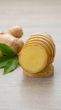Fresh ginger root slices on a light wooden background with green leaves