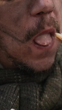 Vertical video of Caucasian homeless young man eating street food hungrily in extreme close up shot. Footage useful for poverty awareness campaigns and charity food donation advertisements