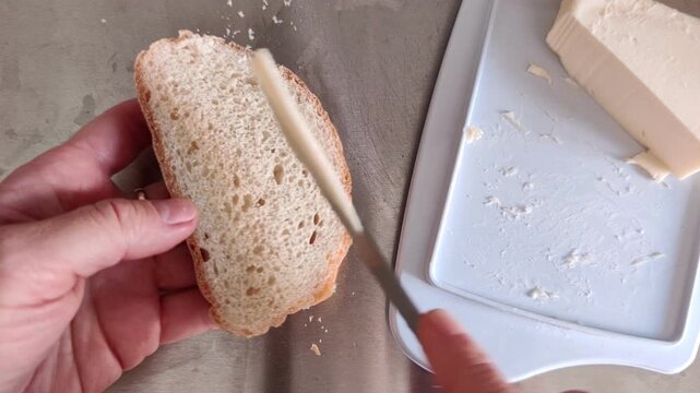 Woman spreading butter on a slice of fresh bread in a bright kitchen