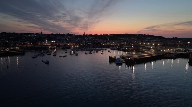 St Peter Port Harbour,Guernsey,Channel Islands. High forward drone footage at dusk over glossy calm water of the harbour ,with full view of whole harbour and glorious sunset over town