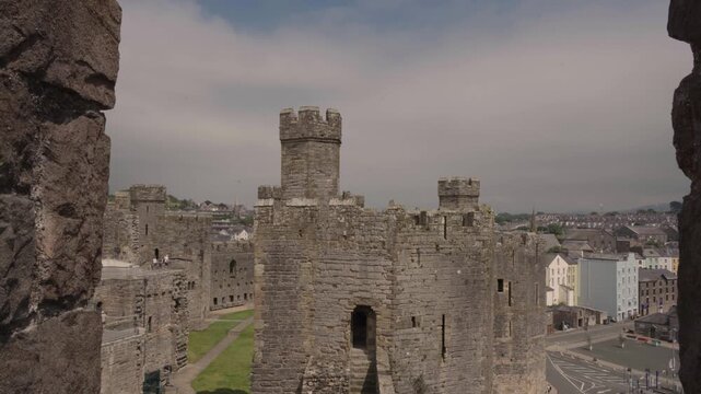Static shot of castle towers framed by greenery around Caernarfon Castle, combining natural and architectural beauty. The contrast highlights the setting.
