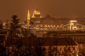 Obraz premium Illuminated Hungarian Parliament and Szechenyi Chain Bridge glowing golden against an atmospheric, misty night sky in Budapest.