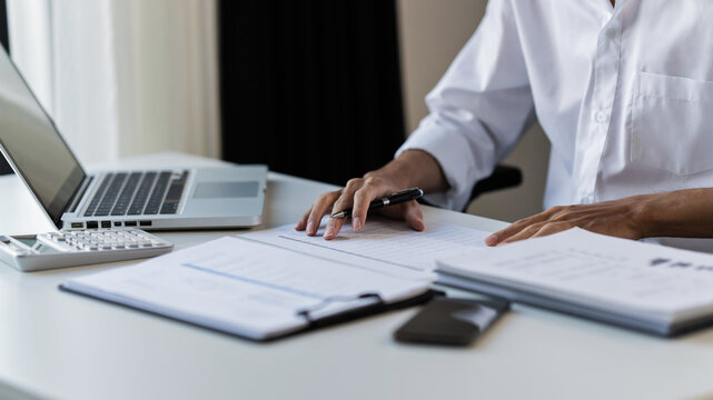 Business executive examining financial data and reviewing paper documents with notebook and pen at office