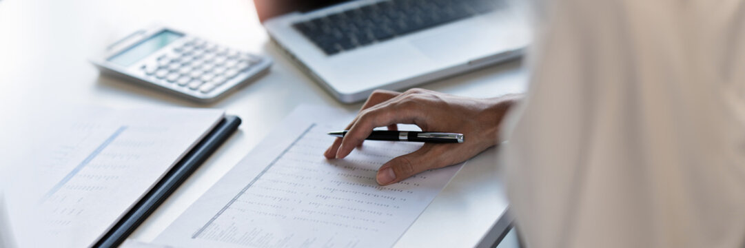 Business executive examining financial data and reviewing paper documents with notebook and pen at office