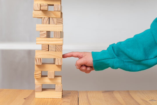 Child's hand carefully pushing a wooden block from a tall tower, demonstrating concepts of balance, risk, strategy, and careful decision making in a tabletop game