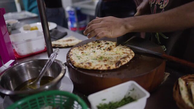 Chef Slicing Fresh Naan Bread with Cleaver on Wooden Board