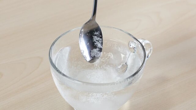 Pouring Spoonful of White Sugar into Glass Cup of Water