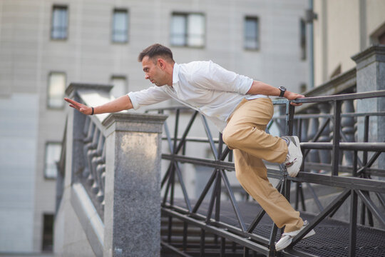 Dynamic young businessman in casual clothes jumping over barrier on city bridge with copy space