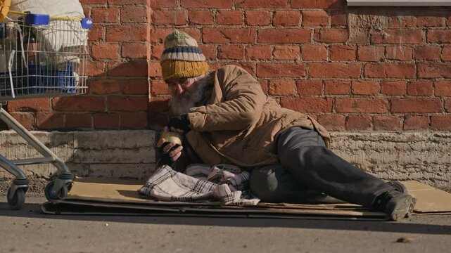 Senior Caucasian homeless man begging on sidewalk and receiving donation from passerby. Perfect for charity campaigns, social welfare documentaries and poverty awareness videos