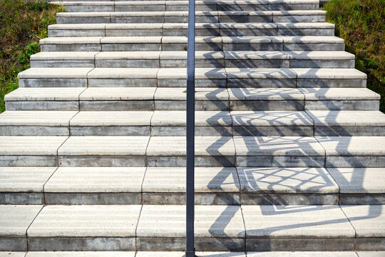 Outdoor concrete stairs with metal handrail casting geometric shadows on sunny day