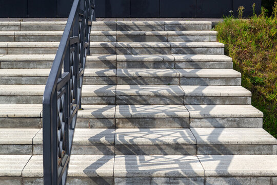 Outdoor concrete stairs with decorative metal railing casting geometric shadows on sunny day