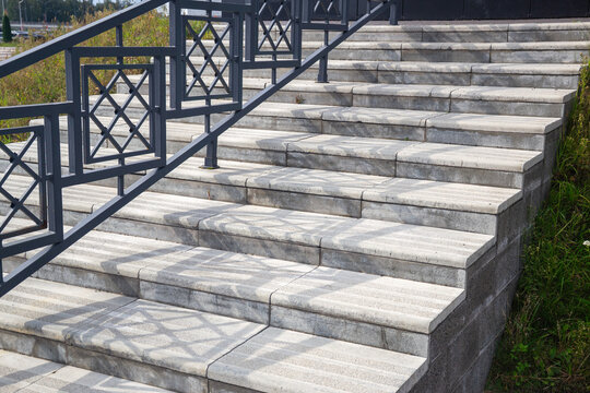 Concrete steps with tactile paving and decorative metal railing casting sharp geometric shadows on sunny day
