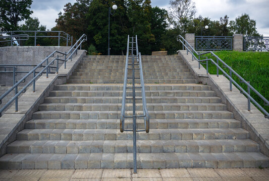 Symmetrical wide angle view of public outdoor stone staircase with central metal handrails on cloudy day