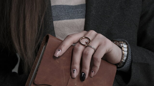 Elegant woman's hand with manicure, rings and wristwatch holding a brown leather notebook