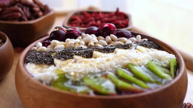 Colorful breakfast bowl fills frame with kiwi slices, chia seeds, coconut and beans. Smoothie bowl looks wholesome and cheerful as honey is poured on top, adding glossy sweetness to rustic tableware.