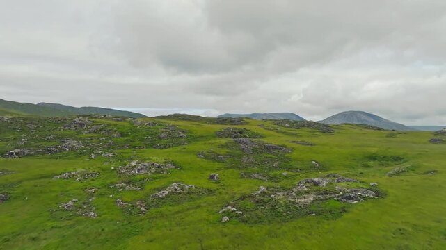 Rocky green upland landscape in Connemara, Ireland, seen in an aerial view with exposed stone, low rounded hills and distant mountains in summer.