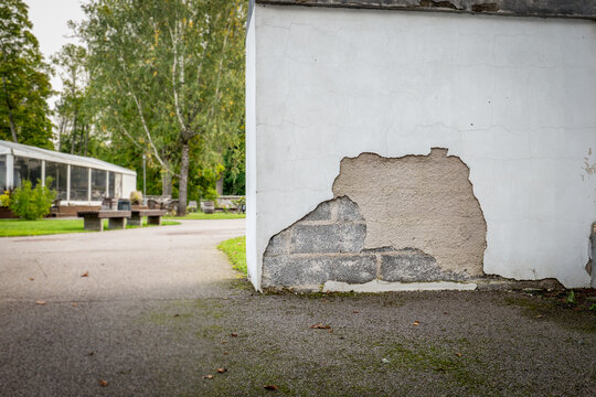 Damaged White Plaster Wall Exposes Masonry Beneath Cracked Facade
