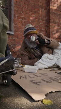 Vertical video of senior Caucasian homeless man receiving hot drink in metal cup outdoors. Perfect for charity campaigns and social welfare documentaries