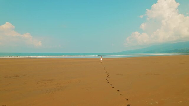 Female tourist leaves footprints on the vast sand beach in tropical Costa Rica