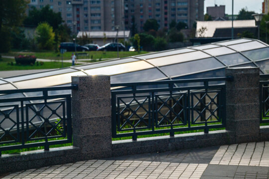 Ornate metal fence with stone pillars along pedestrian pavement near glass canopy structure in city area