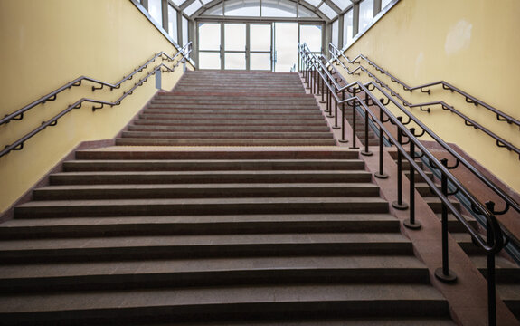 Wide angle view of indoor concrete staircase with metal handrails leading up to glass exit doors of station