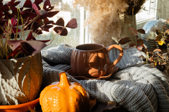 Autumn mood. Mug of coffee or tea on windowsill in cozy interior, raining outside. Warm cozy fall vibes. 