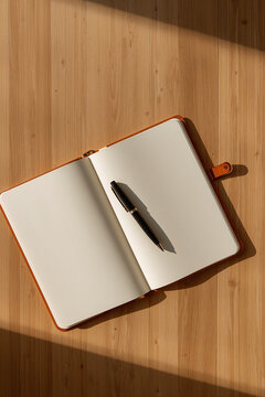 Open blank notebook with pen laying beside it on wooden desk in warm daylight with calm minimalist styling generative AI