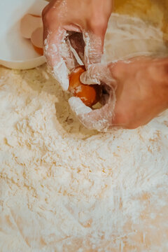 Hands breaking egg into flour for pasta dough close up
