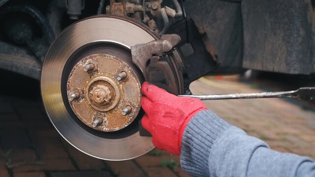 Removing corroded friction pad for inspection during vehicle maintenance. Examining worn braking components on disc rotor assembly outdoors. Automotive repair process focusing on replacement diagnosis