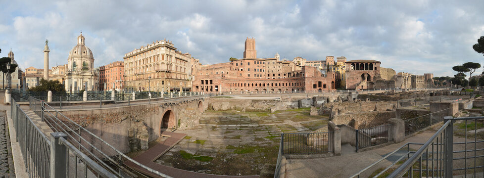 Panoramic view of Trajan market and ancient Roman forum ruins under cloudy sky in Rome.