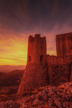 View of Rocca Calascio fortress tower at sunset with warm golden light illuminating the stone walls and rugged mountain landscape in Calascio, Abruzzo, Italy.