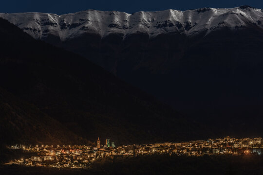 View of the illuminated historic village of Pacentro nestled at the base of snow-capped mountains under a dark night sky in Pacentro, Abruzzo, Italy.