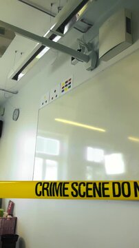 Yellow police tape cordons off an empty classroom with whiteboard, signaling a serious crime scene investigation at a school campus with restricted access and emergency response
