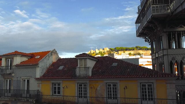 Moving clouds passing over the Lisbon skyline featuring the historic Santa Justa Lift and Sao Jorge Castle on a beautiful day with sunlight reflecting off traditional portuguese buildings
