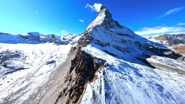 Aerial fpv drone flight towards Matterhorn peak over snowy mountain ridges and steep alpine topography.