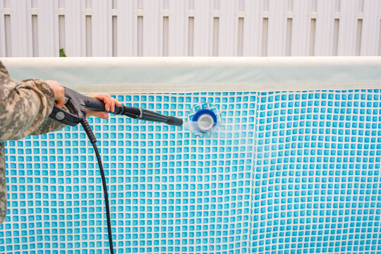 Cleaning a blue vinyl pool liner with a pressure washer.