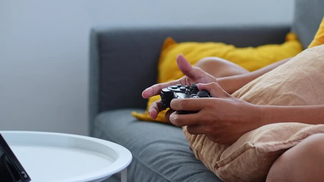 Side angle view of hands playing video games with game pad while relaxing on sofa