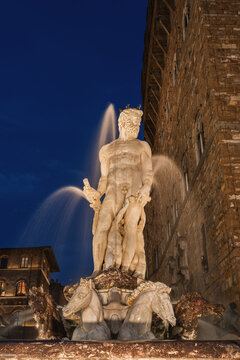 View of the Neptune Fountain with its marble statue illuminated at night in front of the historic Palazzo Vecchio in Florence, Tuscany, Italy.