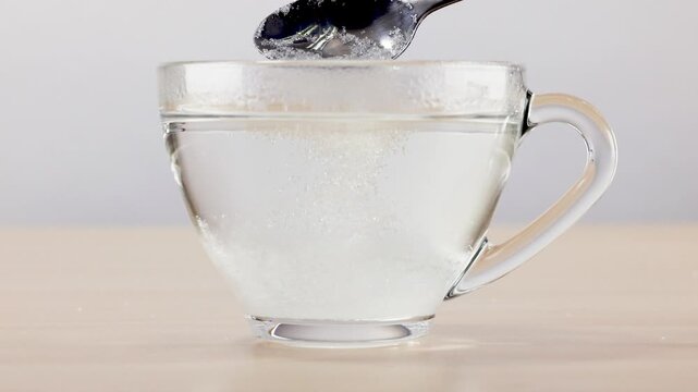 Dissolving Powder in Clear Glass Cup of Water with Metal Spoon