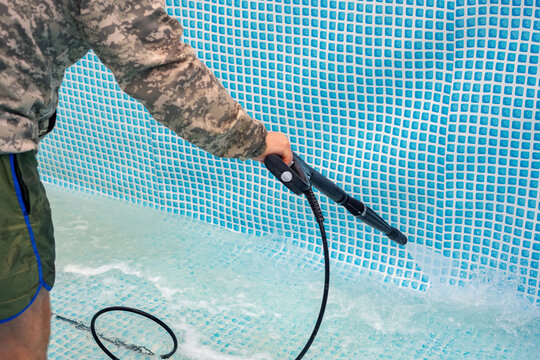 Man cleaning the walls of an above ground swimming pool using a high-pressure water blaster