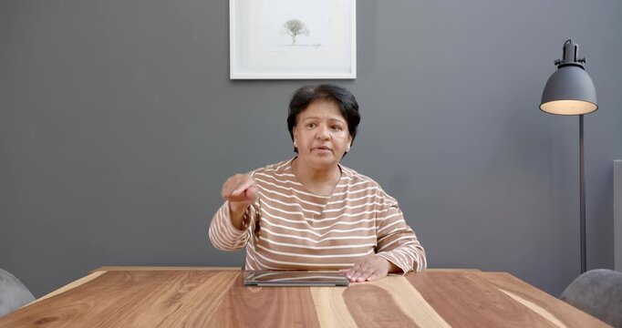 Close up of people talking to the camera, using tablet at home, woman in striped shirt sitting at wo