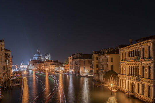 View of the Grand Canal at night with light trails from passing boats and the illuminated dome of Santa Maria della Salute in the distance, Venice, Veneto, Italy.