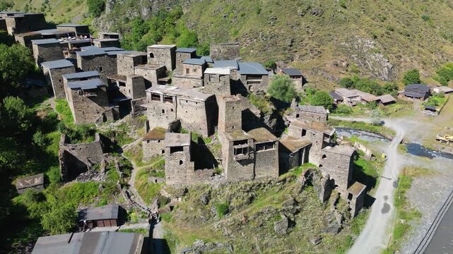 Aerial drone footage rising above Shatili fortress village, changing to a higher view of the stone walls, flat roofs and tightly connected buildings.