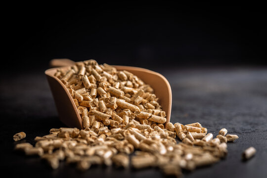 Close-Up of Wood Pellets in a Scoop Spilling Onto a Dark Surface for Heating Fuel