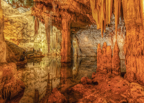 View of the impressive stalactites and stalagmites reflecting in the calm water of a limestone cave in Sardinia, Italy.