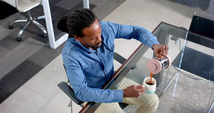 Smiling man enjoying coffee break at office desk with glass tabletop