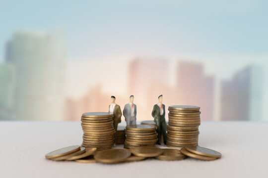 stack of coins in soft focus with blurred miniature business men and city background
