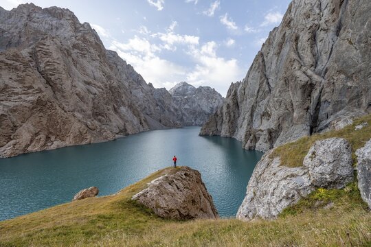 Tourist at the blue mountain lake between rocky steep mountain peaks, Kol Suu Lake, Sary Beles Mountains, Naryn Province, Kyrgyzstan