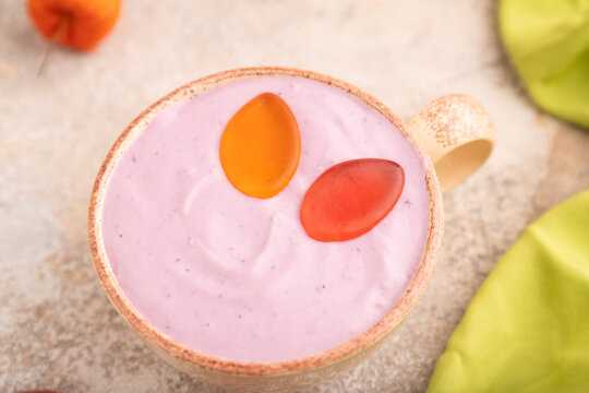 Purple Yogurt, with jelly candy on brown concrete and green textile, side view, close up, selective focus